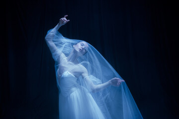Despair. Young graceful balerina in image of ghost bride in art performance isolated on dark background in neon light. © Lustre Art Group 