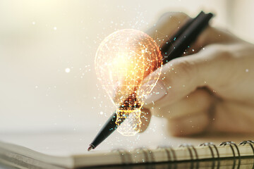 Creative light bulb hologram with hand writing in notepad on background, idea concept. Multiexposure