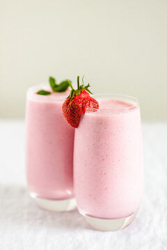 Two glasses of strawberry milkshake with mint and strawberry garnish on table.