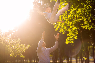 Happy dad throws a laughing son into the sky at sunset with sunshine
