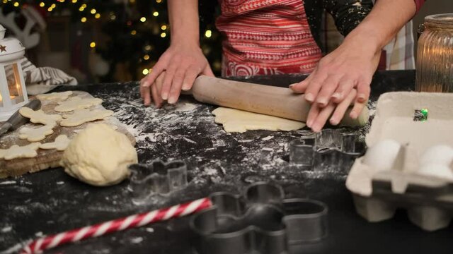 Mother and daughter rolling dough for christmas cookies on table sprinkled with flour