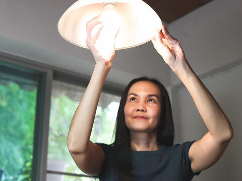 Asian woman  changing light bulb in her house. Selective focus on the lamp.