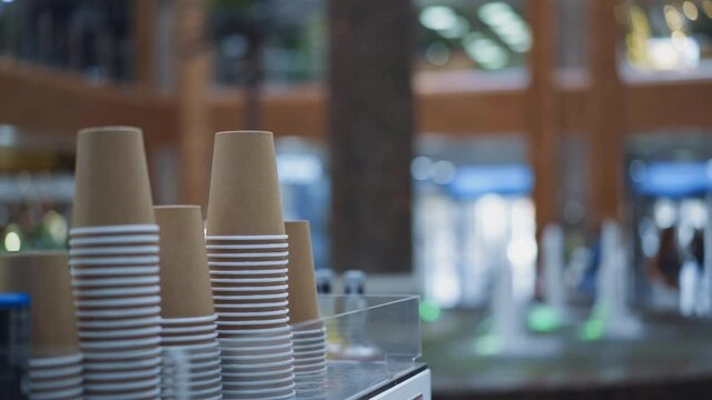 Stacks of beige paper cups on display of cafe against blurred view of fountain in spacious hallway of contemporary shopping mall closeup