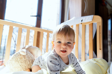 Little kid is kneeling in a wooden crib against the background of a large plush sheep