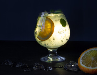 The cocktail glass glows from the inside. Mojito with mint, ice and orange on a black background.