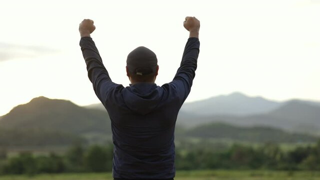 Successful man walking to target and raising arms celebrating at sunset. Sportsman standing happily at the beautiful light. Success, happy concept