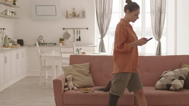 Lockdown of good-looking handicapped Caucasian woman with leg prosthesis sitting down on couch at home and making telephone call