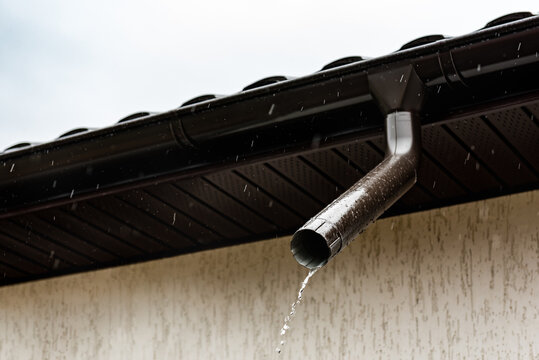 Water flowing from metal downspout during rain.