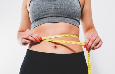 A slender woman measures her waist with a measuring tape. n a white background.