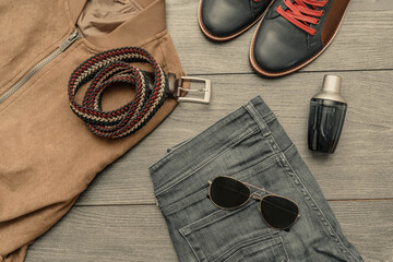 Set of stylish male clothes with shoes, belt, jacket, jeans, sunglasses, perfume on wooden background. Flat lay