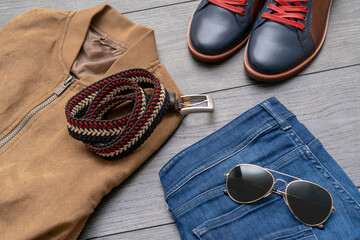 Set of stylish male clothes with shoes , belt, jacket, jeans, sunglasses on wooden background. Flat lay
