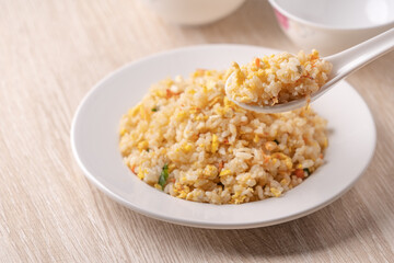 Eating Chinese fried rice in white plate on bright wooden table background.