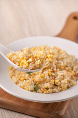 Eating Chinese fried rice in white plate on bright wooden table background.