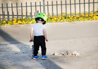Toddler with green bike helmet playing with cobble stones