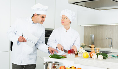 Female and male cooks are making salad on their work place in the kitchen at the cafe.