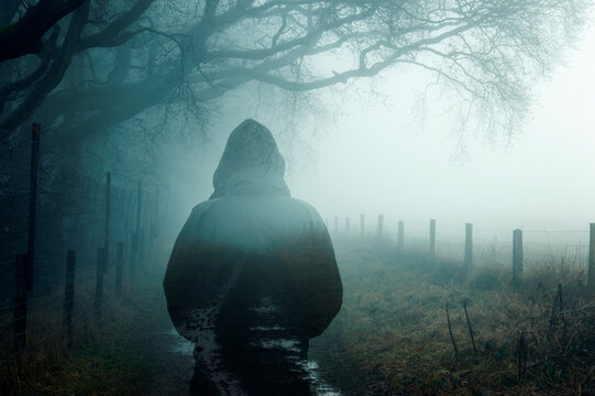 A double exposure of an atmospheric half transparent man looking at a foggy path in the countryside. On a moody foggy winters day.