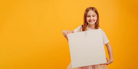 Beautiful girl child holding white canvas and looking at the camera isolated on yellow background...