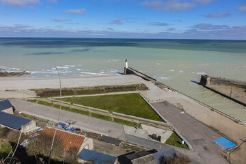 Seawall and pebble beach, lighthouse at entrance to Saint-Valery-en-Caux harbor....