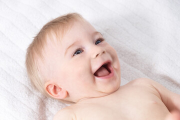 Beautiful caucasian blonde baby girl, infant lying on bed, laughing. Happy childhood, baby care concept, close-up