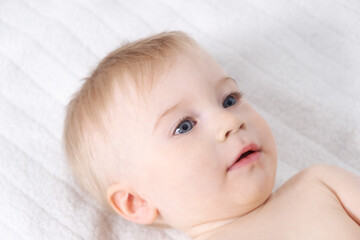 Beautiful caucasian blonde baby girl, infant lying on bed. Happy childhood, baby care concept, close-up