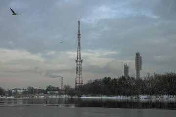 Fototapeta na wymiar On the shore of the lake with ice is a cell tower. The stadium's floodlights and the CHPP pipe are visible