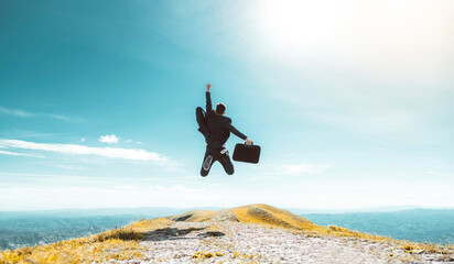 Excited young businessman jumping keeping arms raised hiking the mountain peak - Celebrating...