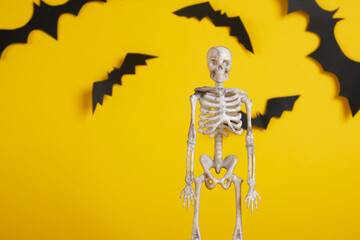 plastic skeleton on a yellow background, cut out from black paper bats, copy space