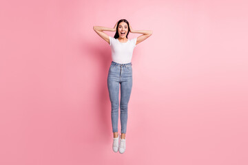 Full size photo of impressed brunette lady jump wear white t-shirt jeans sneakers isolated on pastel pink color background