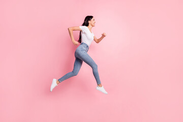 Fototapeta na wymiar Full size profile photo of optimistic brunette lady jump go wear t-shirt jeans sneakers isolated on pastel pink color background