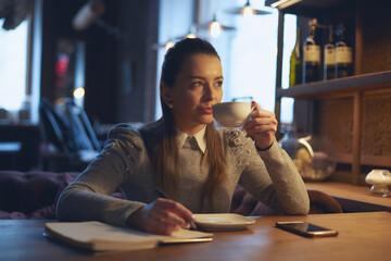 Beautiful woman sitting in a cafe at a table drinking tea and making notes in a notebook