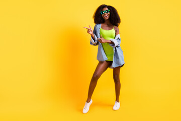 Full length body size view of attractive trendy cheerful girl demonstraing copy space isolated over bright yellow color background
