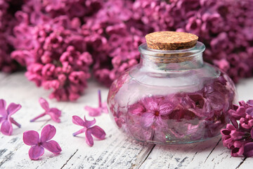 Bottle of oil or infusion from lilac flowers on white wooden table. 