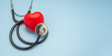 A stethoscope and a red heart laid isolated on a light blue background. Close-up photo. Side view. Space for text. Healthcare and medicine concept