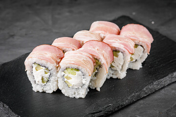 appetizing sushi roll with philadelphia cheese cucumber and bacon on a black stone plate