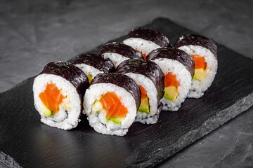 appetizing sushi roll futomaki with cucumber and salmon on a black stone plate