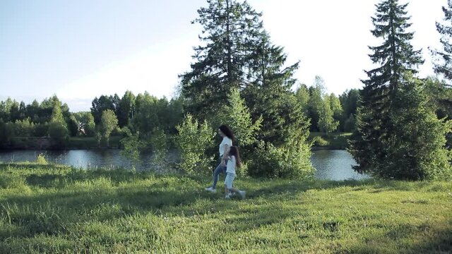 Mom and daughter are walking on the shore of the lake in the summer in a clearing among the trees