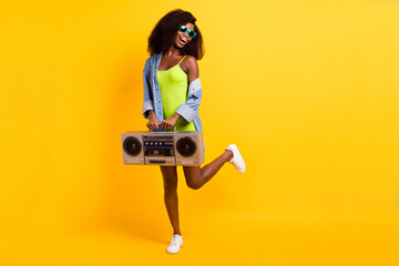 Full length body size photo of girl in sunglass laughing keeping retro tape recorder isolated vibrant yellow color background