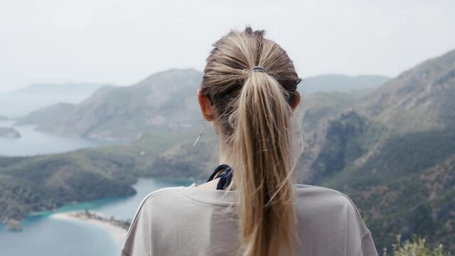 Back iew of calm woman on top of a beautiful mountain valley enjoying the outdoor scenery