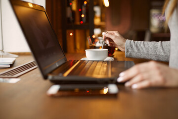 Girl ordering tea in a cafe. Works for a laptop. The mobile phone is on the table. Remote work and freelance work concept.