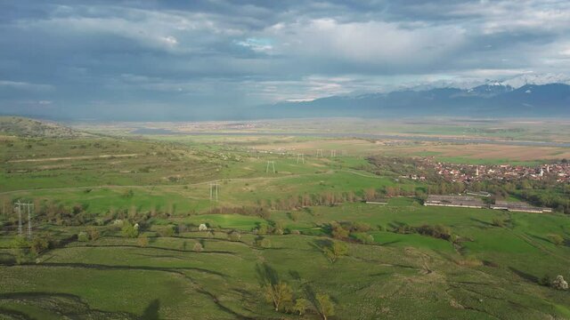 Aerial drone flight above a rural region near Olt river at sunset. Grassy hills, sheep flocks, farms, storm clouds and sunlight create a beautiful countryside landscape. Romania.