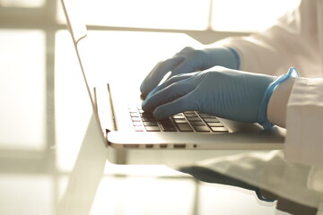 Doctor in blue gloves typing on a laptop in a hospital room