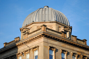 Fototapeta na wymiar Metal Clad Dome & Ornate Roof Line of Victorian Stone Building against Blue Sky