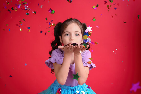 Adorable little girl blowing confetti on red background