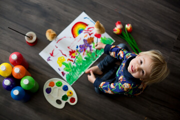 Sweet toddler blond child, boy, painting with colors, little chicks walking around him, making funny prints