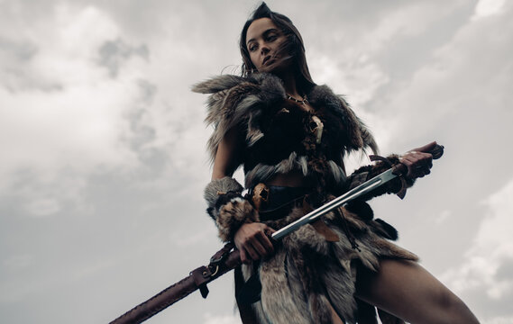 Woman stands in image of warrior amazon with sword in her hand.