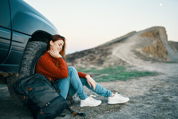 the traveler sits near the car in nature in the mountains and a backpack on the side