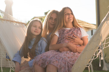 A mother is enjoying her time outside on a hammock swing with her beautiful daughters.