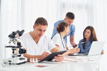 Man with microscope. Group of young doctors is working together in the modern office