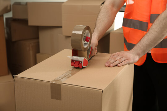 Worker taping cardboard box indoors, closeup view