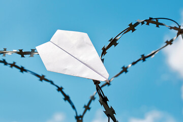 Paper plane stuck in barbed wire against blue sky. Plane hanging in barbed wire. Restricted flights...